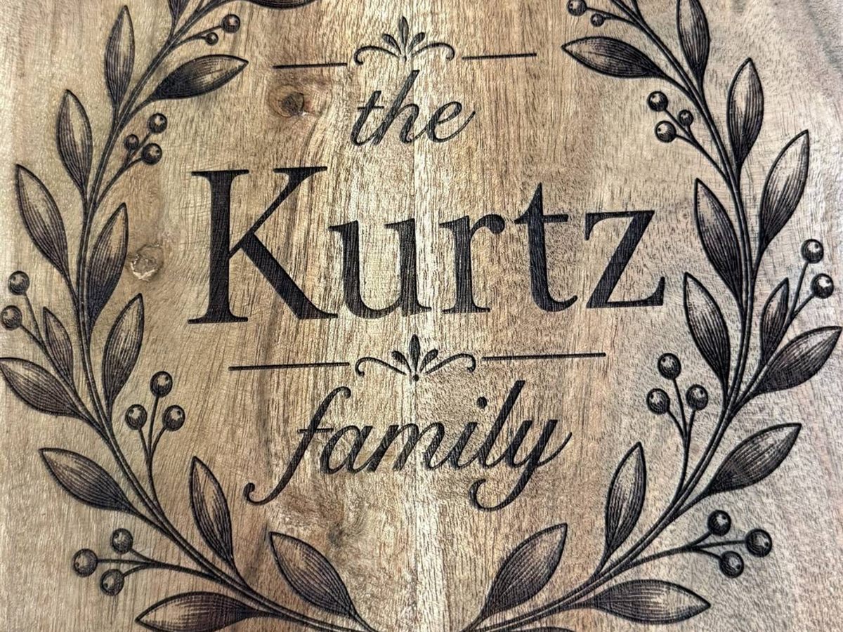 Close view of an acacia board engraved with 'the Kurtz family' inside a laurel wreath