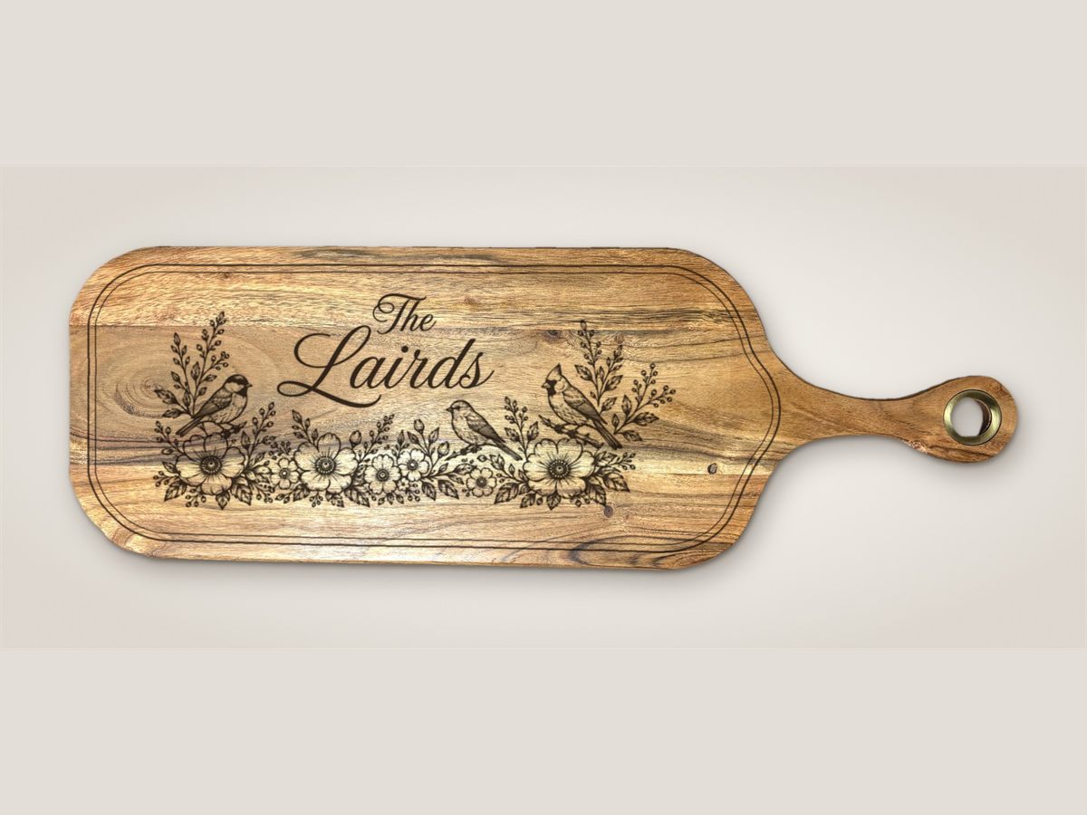 Acacia paddle serving board engraved with 'The Lairds', three songbirds, and a band of wildflowers